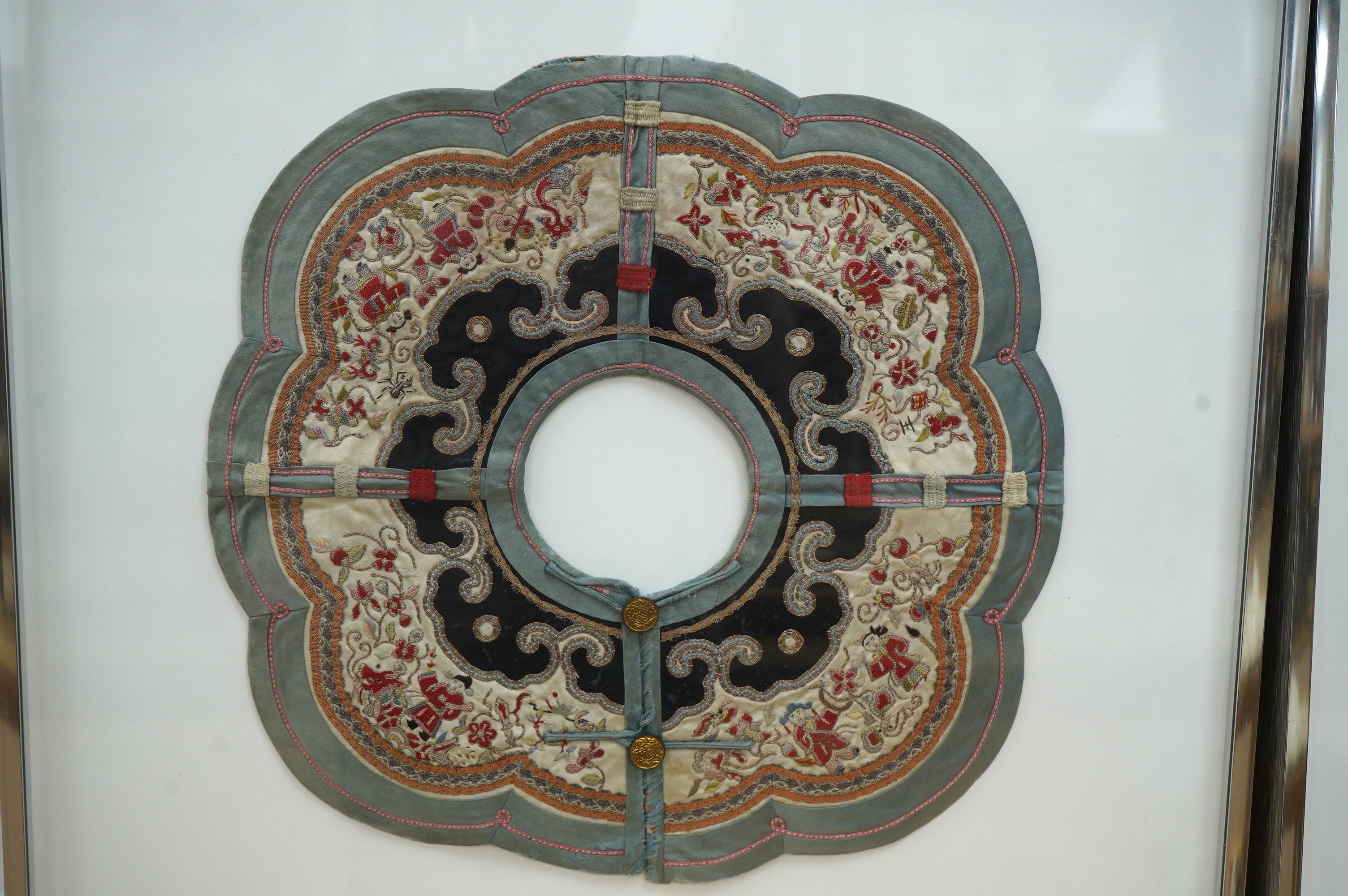 An unusual framed Chinese embroidered cloud shaped child's collar, embroidered with figures and auspicious symbols, in multi-coloured silks and gold thread, edged with braiding and a green silk border, collar 35cm wide.